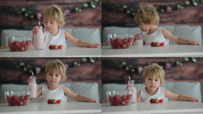 可爱的蹒跚学步的孩子，金发男孩，在家喝冰沙和烤草莓