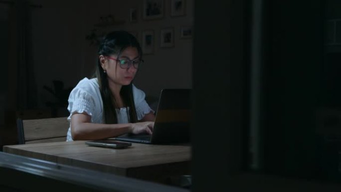 年轻的亚洲妇女正在打字电脑笔记本电脑，并在晚上在家工作，检疫冠状病毒Covid 19大流行作为新的正