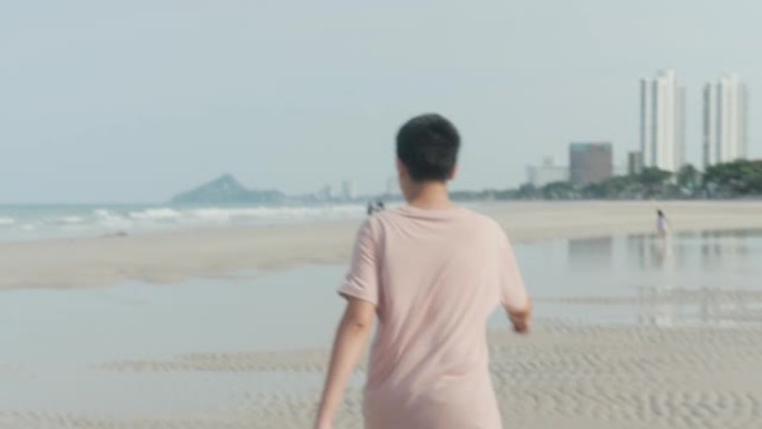 快乐的亚洲男孩在海滩上举手，同时在假期和家人一起放松，生活方式理念。