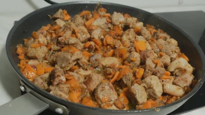 在一个大煎锅中，肉和蔬菜用意大利语油炸。好胃口。角度透镜。洋葱、胡萝卜和香料炒肉。