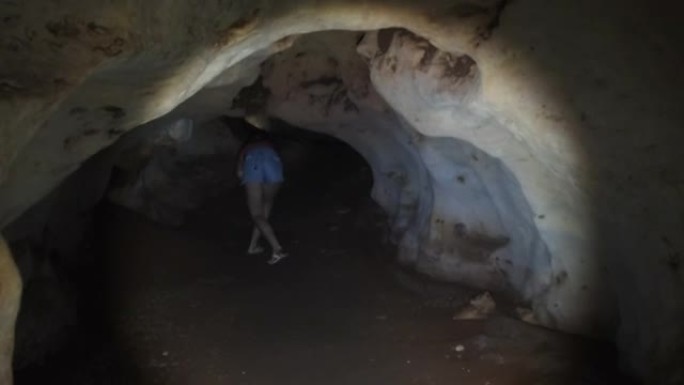 女人在一个深沉的黑暗洞穴中探索钟乳石，用手电筒照亮
