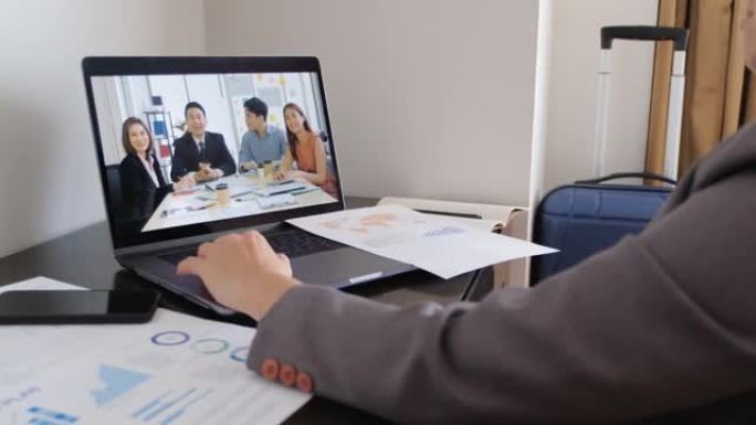 亚洲女商人视频会议通过笔记本电脑上的网络摄像头与团队在酒店房间举行。商务旅行概念