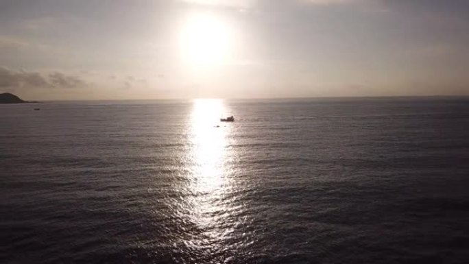 无人驾驶飞机的视野，闪闪发光的太阳升起在海洋地平线上，船漂浮在海面上反射阳光。在旭日照耀下航行的当地