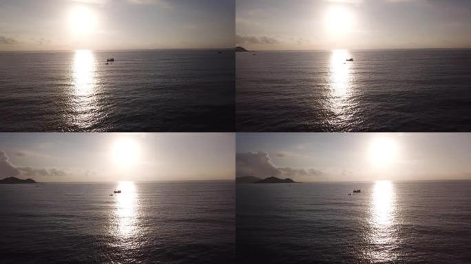 无人驾驶飞机的视野，闪闪发光的太阳升起在海洋地平线上，船漂浮在海面上反射阳光。在旭日照耀下航行的当地