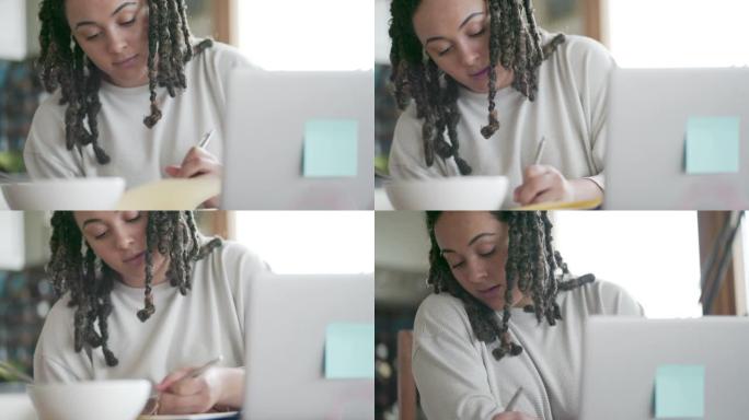 一名年轻女子在家中用笔记本电脑在笔记本上写字