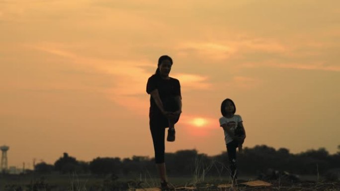 母亲和女儿在日落时在湖上从事瑜伽。家庭深情的关系概念。