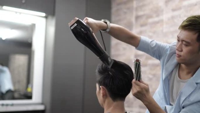 亚洲中国理发师，在他的沙龙里烘干和造型男人的头发。