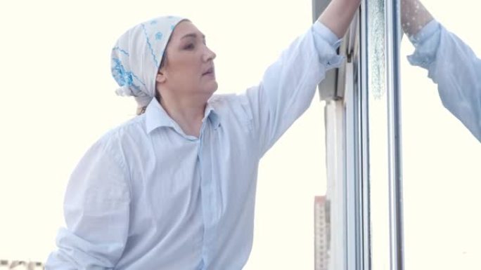 围着围巾的女人的侧视图用抹布洗窗户