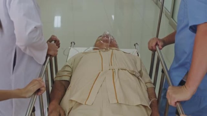 一组医生，护士和外科医生将严重受伤的病人躺在担架上穿过医院的走廊。医务人员急忙将急诊老病人搬进手术室