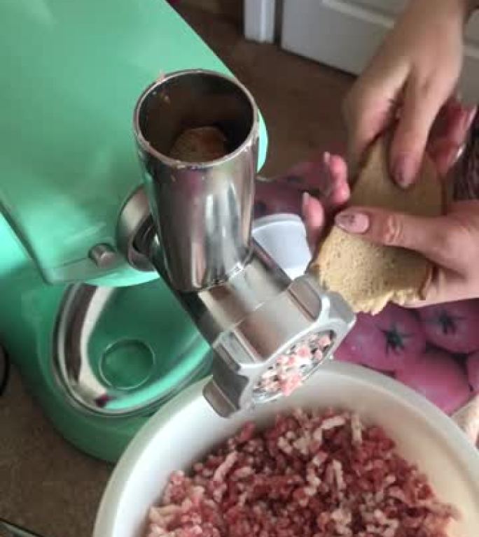 一名妇女在食品加工机上准备肉末。添加面包。碎肉掉进碗里。