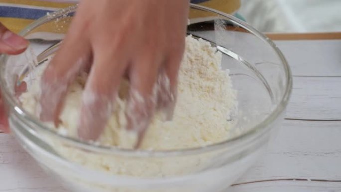 孩子的手在桌子上的搅拌碗中脱粒面粉，制作面包。