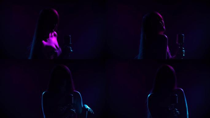 迷人的女歌手在派对上用复古麦克风表演现场音乐。在黑暗的工作室里，一位长发被蓝色和紫色灯光照亮的艺术家