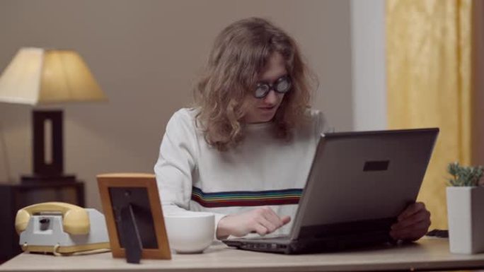 使用复古笔记本电脑在家工作的认真集中的年轻20世纪80年代男子的肖像。聪明的高加索人在室内对老式过时