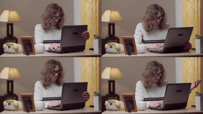 使用复古笔记本电脑在家工作的认真集中的年轻20世纪80年代男子的肖像。聪明的高加索人在室内对老式过时