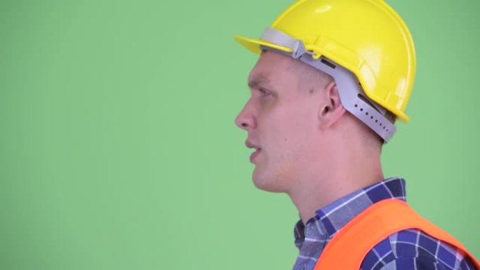 男子建筑工人面对绿色背景谈话的侧面图
