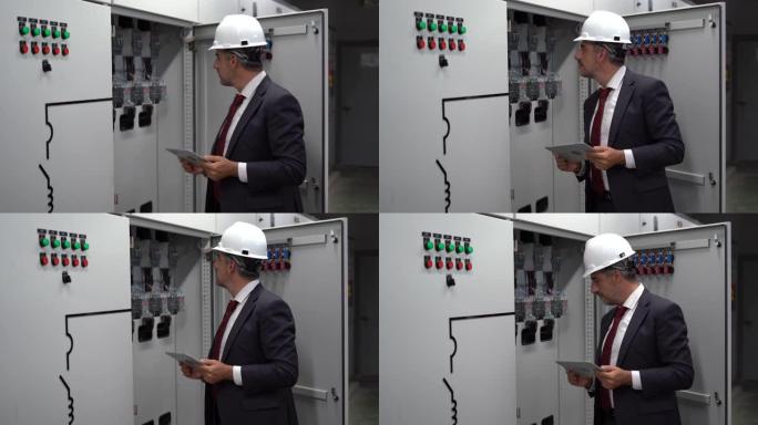 工业工程师经理使用数字平板电脑在工业制造工厂检查带有控制面板的电气开关齿轮柜的信息和安全系统。商人检