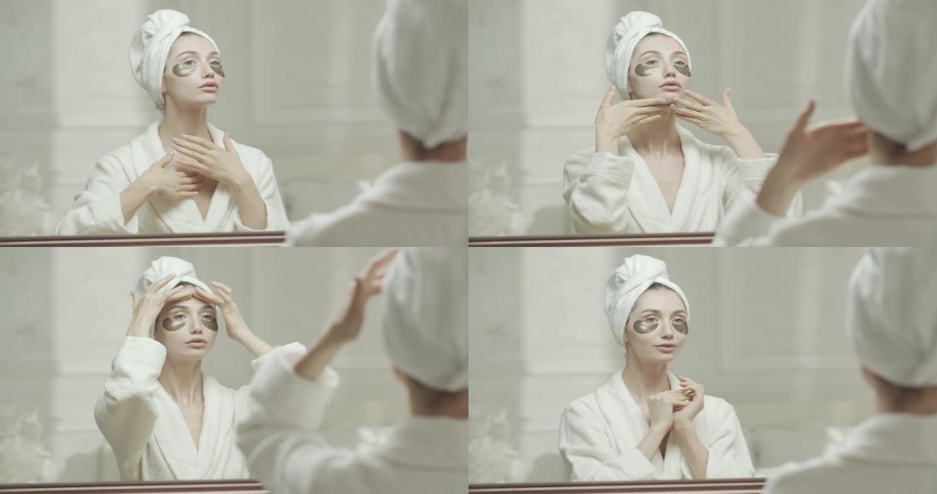 穿着浴袍和毛巾的年轻女子，看着镜子里的自己，用手将保湿霜涂在脖子和脸上。