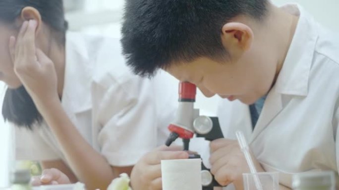 亚洲学童穿着实验服在课堂上与显微镜一起研究，教育生活方式理念。