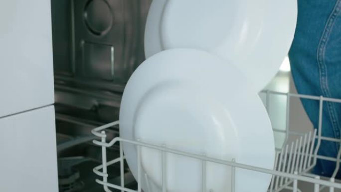 厨房里的一个女人正在把盘子放在洗碗机的拉出式底部抽屉里，并放置白色汤碗。特写