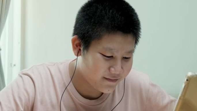 在新型冠状病毒肺炎，检疫和社交疏远的生活方式概念中，亚洲男生在家里的餐桌上通过数字平板电脑学习在线课