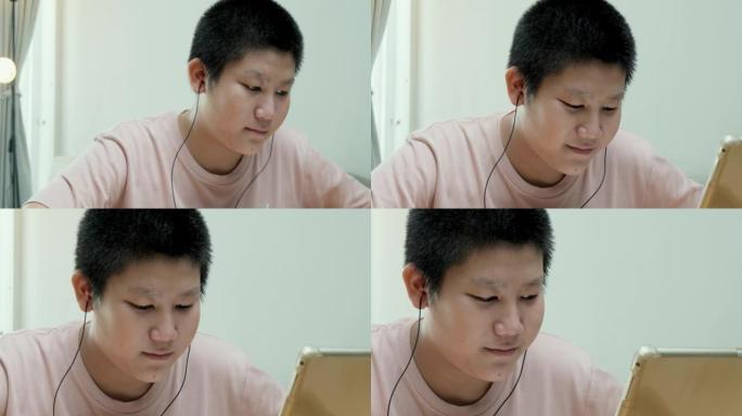 在新型冠状病毒肺炎，检疫和社交疏远的生活方式概念中，亚洲男生在家里的餐桌上通过数字平板电脑学习在线课