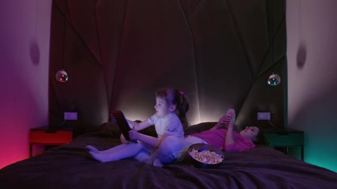 年轻的妈妈和可爱的小孩女儿躺在家里的沙发上使用数字平板电脑技术设备和手机