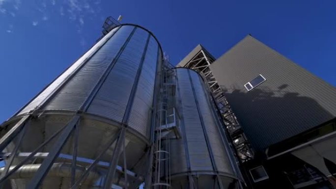 外面的银色容器。蓝天下的现代农业综合体。大型谷物升降机。工业厂房。从下面看。