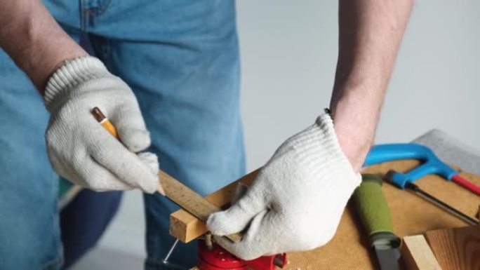 一个戴着防护手套的木匠用铅笔和尺子在一块小木板上标记尺寸。DIY。