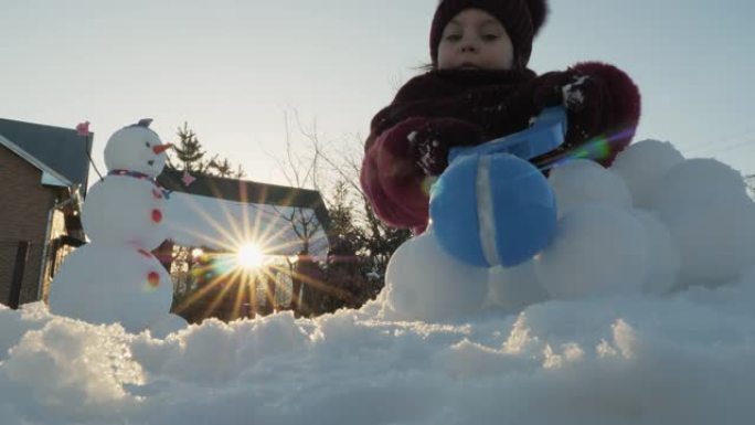 可爱的小女孩在一个有趣的雪人附近打雪球