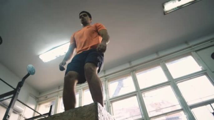 一个年轻的运动型男子在健身房的盒子上跳跃
