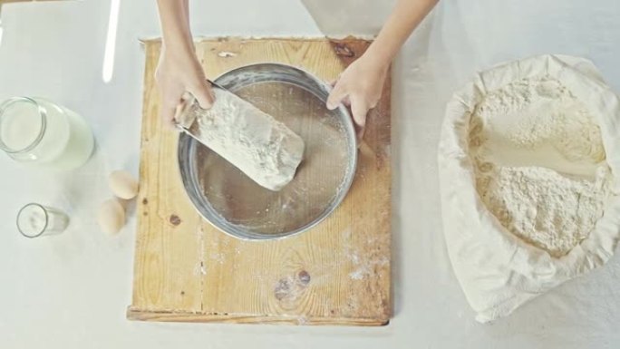 年轻的面包师在面包店以质朴的木制背景筛选面粉。带复制空间的俯视图