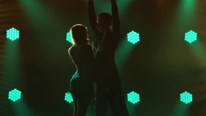 伦巴，桑巴，恰恰，摇摆。一对专业舞者在绿色霓虹灯的背景下，在黑暗的工作室里热情地跳舞。轮廓。特写。慢