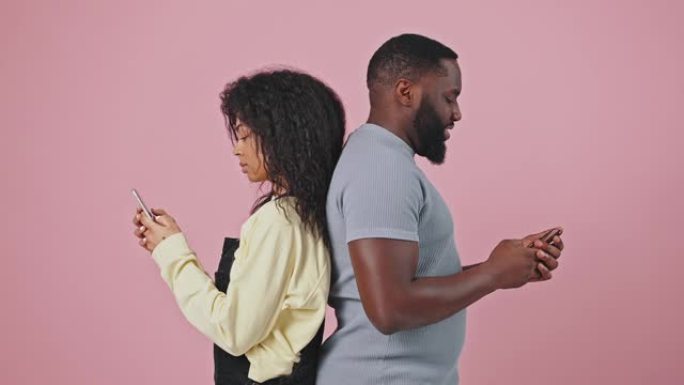 在线约会应用程序。年轻的非洲裔美国男女在智能手机上发短信，背靠背站着，