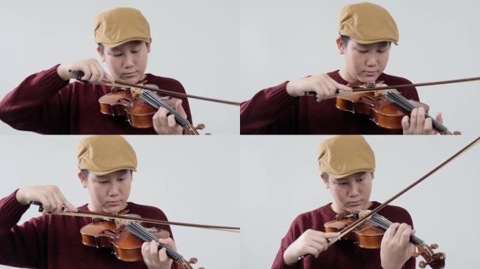 穿着毛衣的亚洲男生学习拉小提琴的灰色背景，生活方式的概念。