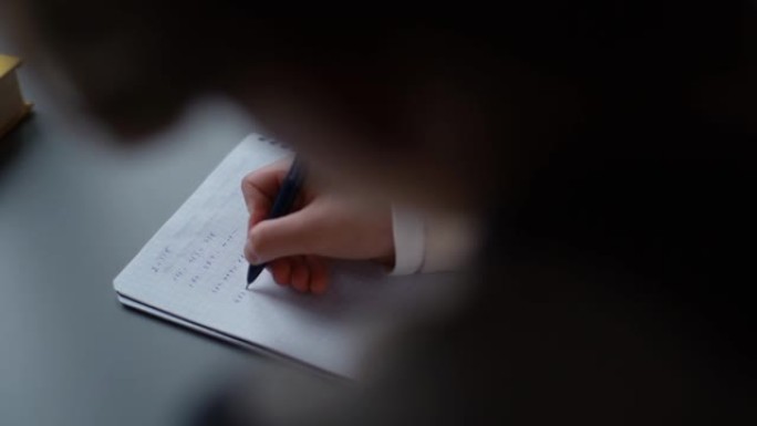 小学生男孩的特写手在纸上写笔记本解决数学方程式坐在家里的桌子上