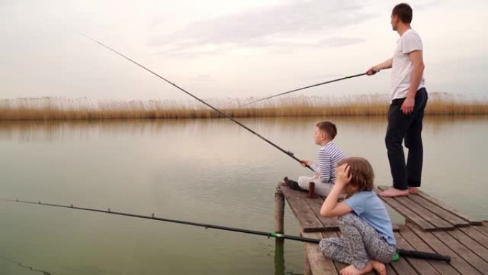 爸爸和儿子和女儿在木桥上从河里抓鱼。