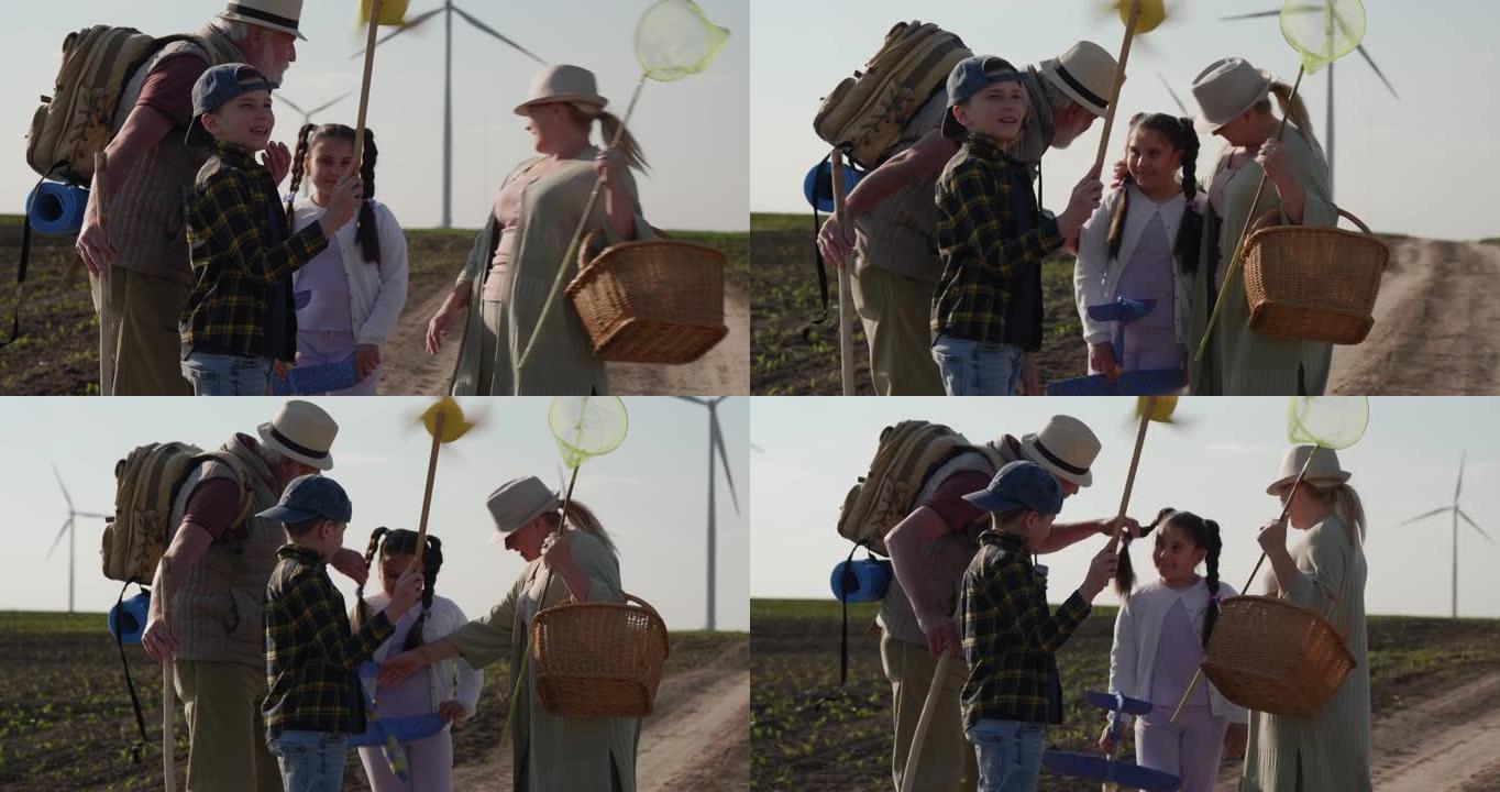 小男孩留着一个小风车玩具，和家人在风车田里玩得很开心。祖父母带着大自然的孙子孙女去野餐，在草地上玩耍