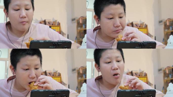 亚洲男生吃炸鸡，在家通过智能手机学习在线课程，新型冠状病毒肺炎，社交疏远的生活方式概念。