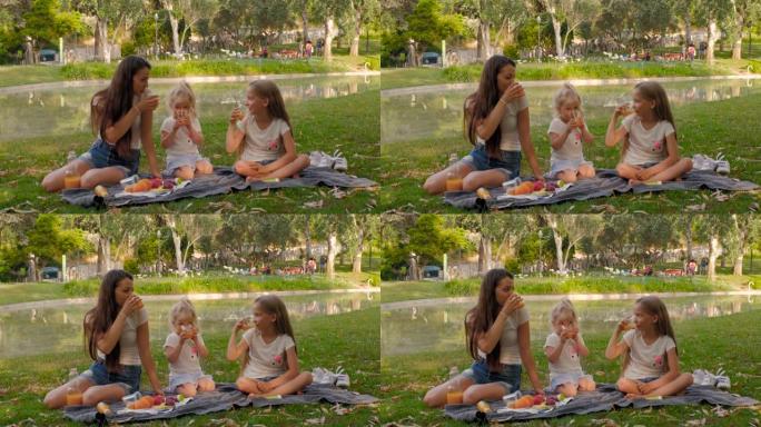 美丽的母女俩在公园里野餐。他们正在享受和喝橙汁。两个小孩和妈妈