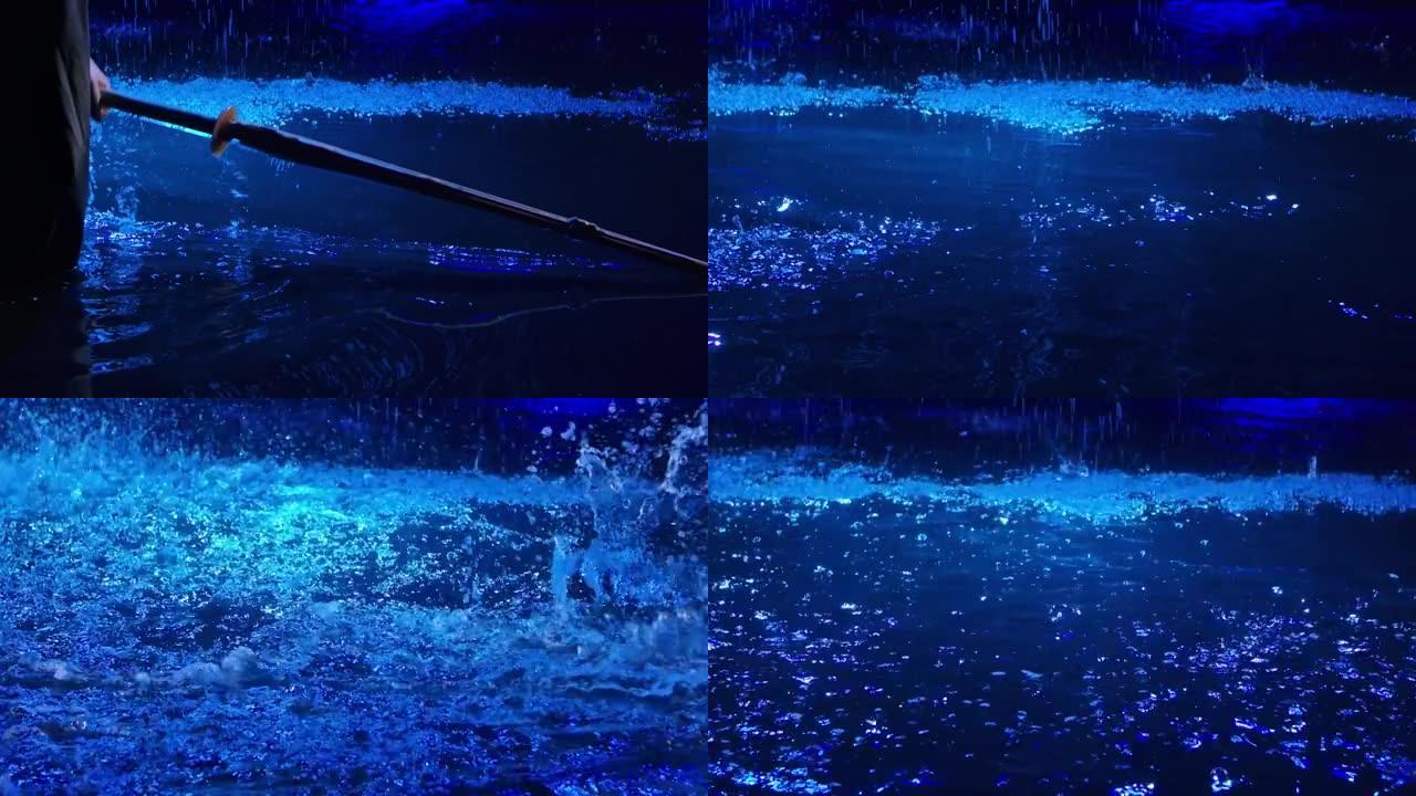 日本剑道战士的竹剑躺在水面上，被蓝光照亮。人举起shinai剑并踏入水中，产生许多飞溅。特写。慢动作