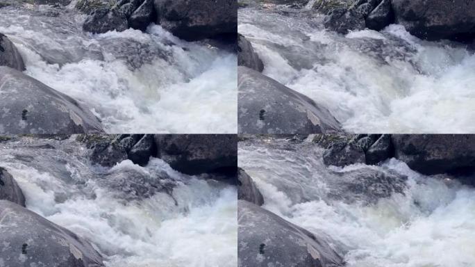在灰色岩石之间涌出水流。石崖布满苔藓。山河在岩石上断裂，形成飞溅和泡沫。水元素的自然动力和能量