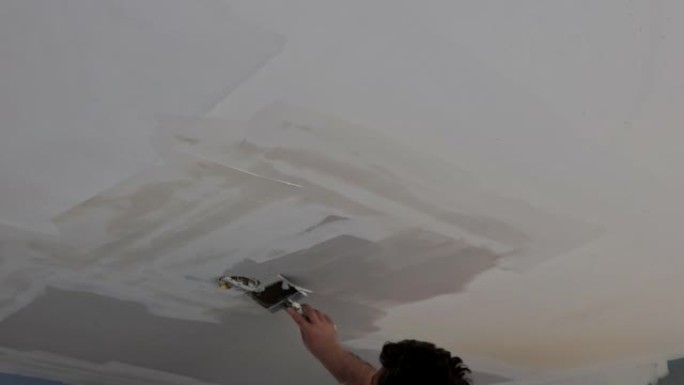 一个男人用刮铲和抹灰石膏纸板天花板对准墙壁的特写镜头