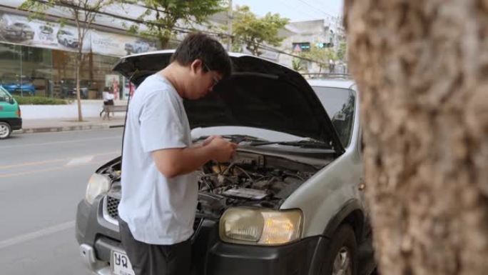 亚洲年轻不快乐的男子在乡村公路上开着的引擎盖抛锚的汽车前用手机通话
