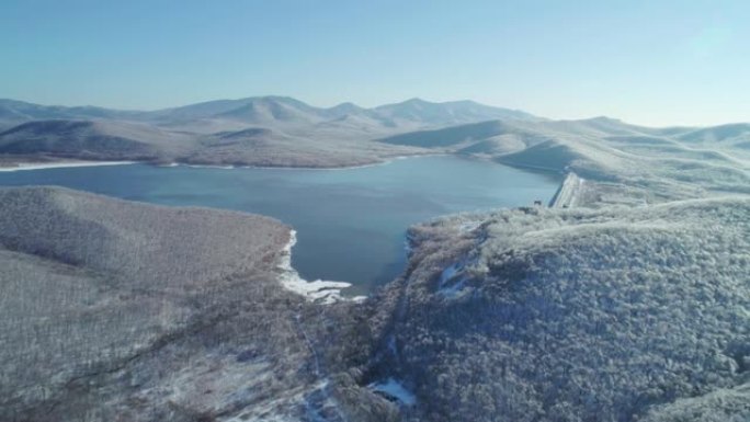 在雪山和冰封森林之间的蓝色湖上鸟瞰图。美丽的冬季风景。