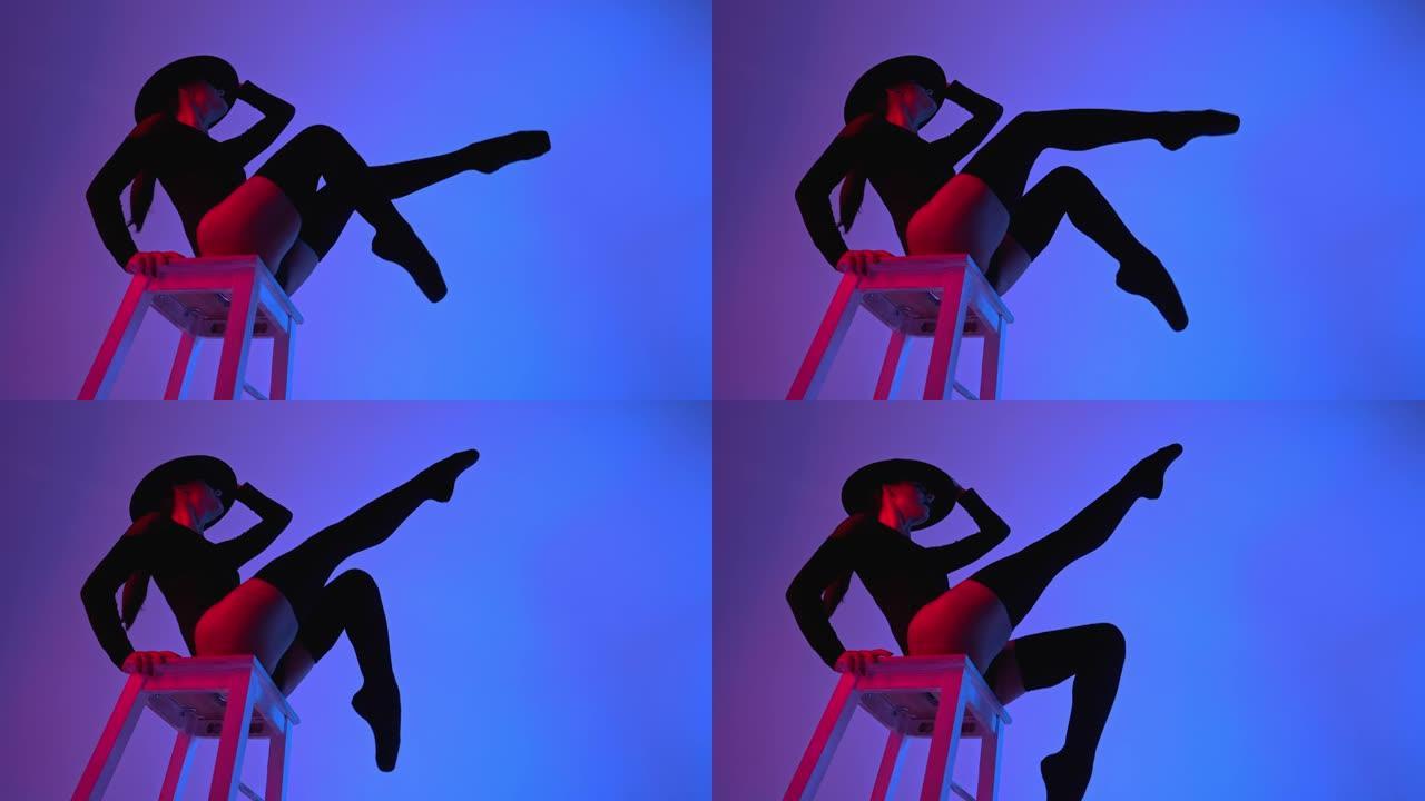 戴着帽子的专业芭蕾舞演员坐在紫色霓虹灯下的多色背景上的高脚椅上。性感性感的芭蕾舞演员穿着长筒袜跳舞。