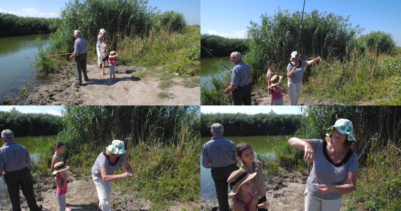 在温暖的夏日里，穿着休闲服的活跃快乐健康的欧洲老年夫妇和他们的两个孙女在湖边用鱼竿钓鱼。慢动作4k 