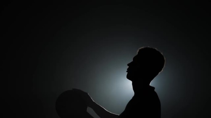 一个年轻的篮球运动员在黑暗的工作室背景上练习投掷的剪影，带有烟雾和背光。特写。侧视图。慢动作准备59