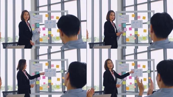 亚洲女商人领袖用图表和图表进行活动挂图演示，并在董事会会议室进行讨论，商人拍手，同时在商业工作计划中