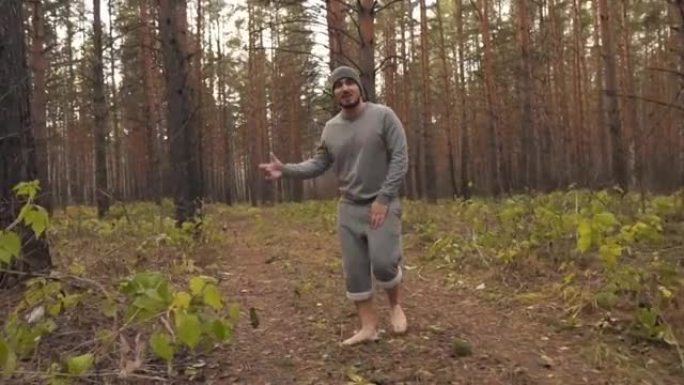 一个赤脚的男人在秋天的森林里唱歌说唱，握着手，看着相机。加速视频