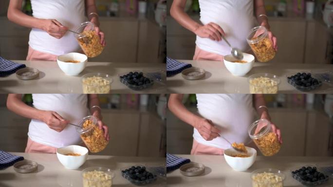 孕妇在家里做早饭玉米片谷类食品，并在厨房里添加配料。制作富含纤维和营养的健康有机餐